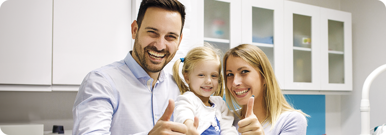 A happy family with a young child giving thumbs up in a dental clinic, highlighting a positive experience with family dental care.