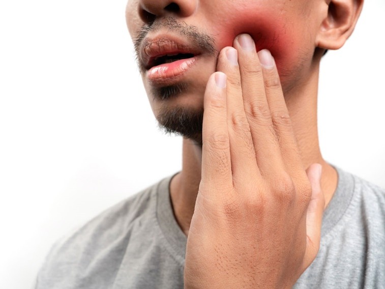 A man touching his swollen, red cheek, indicating pain or discomfort, possibly due to a dental or oral issue.